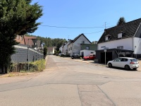 Breite Einfahrsstraße an einer Kreuzung ohne einen sichtbaren Gehweg.