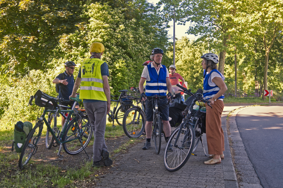 Eine Gruppe von Menschen mit Fahrrädern pausieren ihre Radtour an einem begrünten Ort.