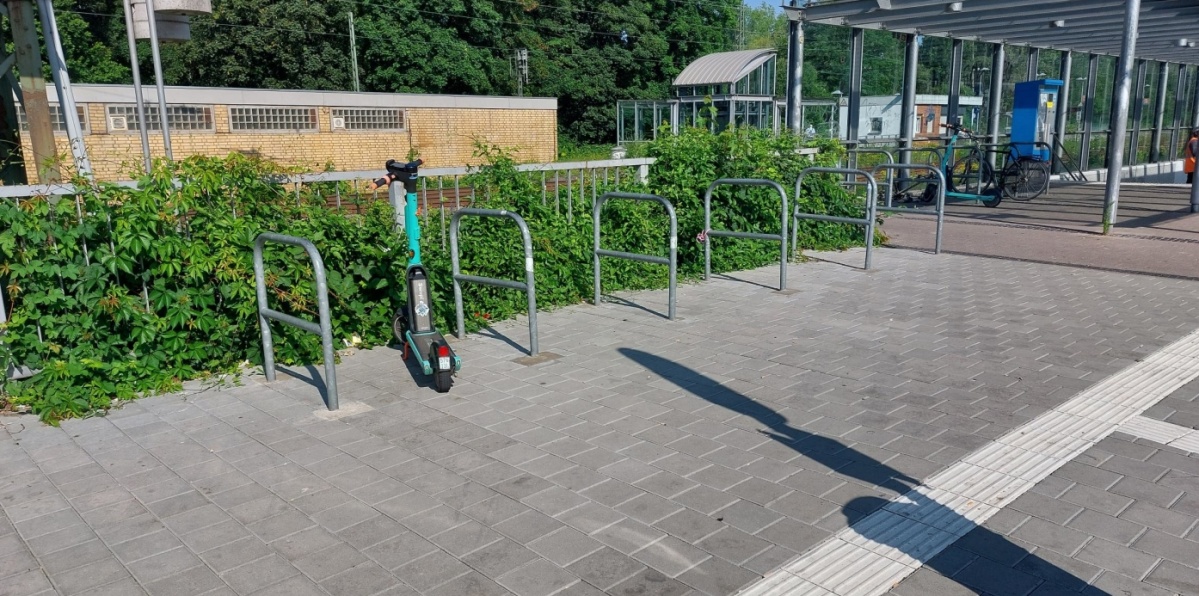 Eine Reihe an Radbügeln, zwischen denen ein E-Scooter steht.