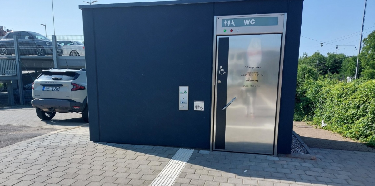 Toilettenhäuschen von außen mit dem Hinweis auf ein barrierefreies WC.